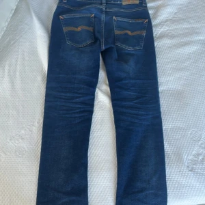 Nudie jeans Grim Tim - Säljer ett par snygga blå jeans från Nudie Jeans, modell Grim Tim. Storlek: w28 L30 De är tillverkade i 99% bomull och 1% elastan för en bekväm passform. Jeansen har en klassisk femficksdesign och orange sömmar som ger en cool kontrast. Använda men mycket väl omhändertagna. 