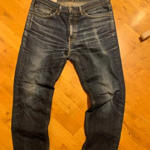 Levi's 541 mörkblå jeans selvadge - Säljer ett par Levi's 541 selvadge jeans i mörkblå tvätt med snygga slitningar och klassiska fem fickor. Jeansen har raka ben och normal passform, med gul kontrastsöm och detaljerade nitar. Perfekt för dig som gillar en tidlös look. Riktigt bra skick. Storlek 34/32
