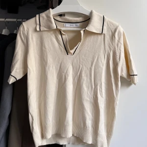 Beige pikétröja med svarta detaljer - 🤍Beige pikétröja från Mango med svarta tunna ränder på krage och ärmslut. Tröjan har korta ärmar, v-ringad hals och ribbade muddar (liten i storlek, denna är XL men är som en S)🤍