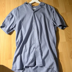 Ljusblå kortärmad skjorta Strömberg - Fräsch ljusblå skjorta från Strömberg i mjukt lyocell-material. Skjortan har korta ärmar, klassisk krage och knappar framtill. Perfekt för dig som gillar stilrena och enkla plagg med skön passform.