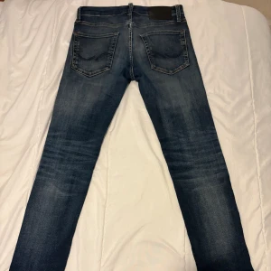 Jack & Jones Slim Fit Glenn jeans - Snygga blå jeans från Jack & Jones i modellen Slim Fit Glenn. Jeansen har klassisk femficksdesign, knappgylf och slitningar som ger en cool, tvättad look. Passformen är slim och materialet är mjukt denim med lite stretch för extra komfort. Finns ett hål vid gylfen, se bild. 