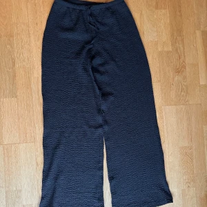 Vida byxor - Säljer ett par super coola svarta reflade vida byxor från H&M Divided i storlek XS. Byxorna har en bred passform med struktur i tyget och snörning i midjan. Materialet är mestadels polyester med lite elastan för stretch. Perfekta för dig som gillar bekväma och trendiga byxor. I nyskick, endast använda två gånger. Innerbenslängd: 78cm. Nypris: 200kr. Säljer för: 80kr!