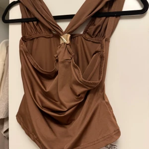 Brun korsett-topp från SHEIN - Snygg brun korsett-topp från SHEIN med coolt guldfärgat metallspänne framtill. Toppen har breda axelband och en draperad look som ger extra edge. Materialet är mjukt och stretchigt, perfekt för att skapa en trendig siluett. Passar dig som gillar statement-plagg och vill sticka ut.