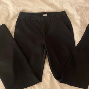 Svarta kostymbyxor med rak passform från Lindex  - Snygga svarta kostymbyxor med klassisk rak siluett och diskreta fickor i sidorna. Byxorna har bälteshällor och är perfekta för en clean och stilren look. Materialet känns mjukt och har en lätt stretch för extra komfort. Från Lindex 