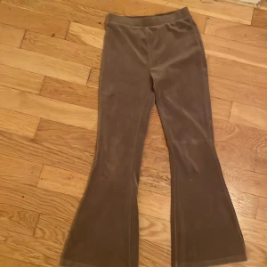 Bruna bootcut byxor från Lindex - Säljer ett par bruna bootcut-byxor från Lindex i mjuk fleece. Byxorna har en skön elastisk midja och är perfekta för dig som gillar retrostil och vill ha något riktigt bekvämt. Materialet är lent och värmande, och färgen är en snygg mörkbrun ton.