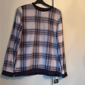 Rutig fleece-tröja i lila och beige - Mysig långärmad fleece-tröja från Cubus i storlek S. Tröjan har ett rutigt mönster i lila, beige och inslag av rosa, med mörka muddar vid ärmslut och nederkant. Perfekt för kyliga dagar och enkel att matcha med jeans eller leggings.