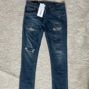 Dondup George skinny jeans blå - Snygga blå jeans från Dondup, modell George Skinny Fit. Jeansen har slitna detaljer och hål på låren och knäet, slitningarna är gjorde i fabrik. Klassisk femficksdesign, knappgylf och smal passform. Nypris 3400 säljer för 1199!
