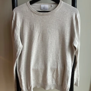Beige stickad tröja från Bläck - En stilren beige stickad tröja från Bläck med rund halsringning och ribbade muddar. Perfekt för lager-på-lager och enkel att matcha med jeans eller chinos. Klassisk passform och mjukt material som känns skönt mot huden. Nypris 600