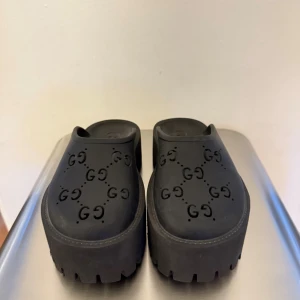 Svarta plattformssandaler från Gucci - Chunky svarta sandaler från Gucci med plattformssula och präglat GG-mönster över hela ovandelen. Tillverkade i syntetmaterial med grov sula för extra edge. Perfekt för dig som gillar statement pieces och vill ha något unikt på fötterna.