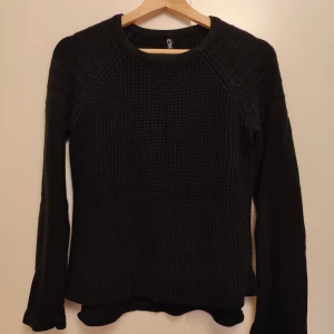 Svart stickad tröja med lång ärm - Svart stickad tröja från Gina Tricot med rund hals och ribbade detaljer på axlarna. Tröjan har lång ärm och en något vågig nederkant som ger en chill vibe. Perfekt för lager-på-lager under kyliga dagar.