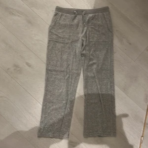 Grå Juicy Couture - Grå mjukisbyxor från Juicy Couture med bred resår och snörning i midjan. Stora fickor fram med broderad JC-logga och bakfickor med knappdetaljer. Mjukt material som känns skönt mot huden, perfekt för chill dagar.