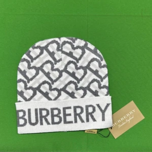 Vit och grå Burberry mössa förbeställ tt:Marknads.closet - Snygg vit och grå mössa Burberry med ikoniskt mönster och stor logga framtill. Mössan har en uppvikt kant och är tillverkad i mjukt stickat material. Perfekt accessoar för att lyfta din vinterstil.