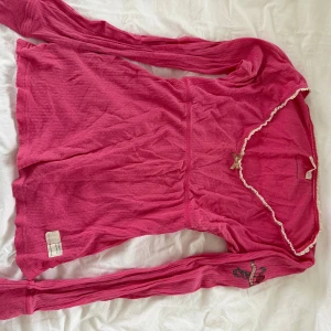 Rosa långärmad topp med rosett  - Supersöt rosa långärmad topp från Odd Molly med liten rosett och spetskant vid urringningen. Toppen har broderad detalj på ena ärmen och är tillverkad i mjuk bomull.  Passar Xs-S