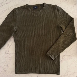 Olivgrön grovstickad tröja Jack & Jones - Snygg olivgrön grovstickad tröja från Jack & Jones med rund hals och långärmad design. Tröjan har ett diskret, strukturerat mönster som ger en cool textur och passar perfekt till jeans eller chinos. Enkel och stilren modell som funkar året runt. Perfekt skick. 