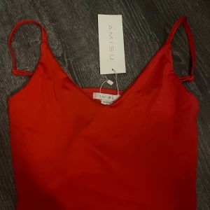 Röd satin klänning från Amisu - Snygg röd klänning från Amisu i satinliknande material med smala axelband och v-ringad hals. Perfekt för dig som vill sticka ut med en enkel men elegant look. Klänningen har en slimmad passform och känns riktigt trendig.