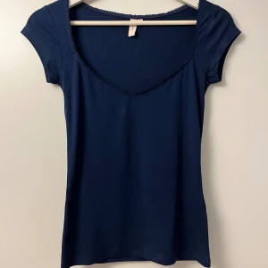 Marinblå topp med v-ringning - Snygg marinblå topp från Nelly med v-ringad hals och korta ärmar. Tunn och mjuk bomullskvalitet