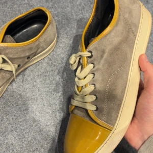Lanvins uk9 - Snygga sneakers i beige mocka med kontrasterande gul lackad tå och gul kant runt öppningen. Skorna har beige snörning och en platt, ljus sula. Perfekt för dig som gillar unika färgkombinationer och vill sticka ut lite extra.