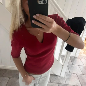 Röd topp med v-ringning - Snygg röd topp med v-ringad hals och trekvartsärm. Modellen är figurnära och passar perfekt till jeans eller kjol. Materialet känns mjukt och stretchigt, vilket gör den bekväm att bära hela dagen. Enkel och stilren design som ger en fräsch look.