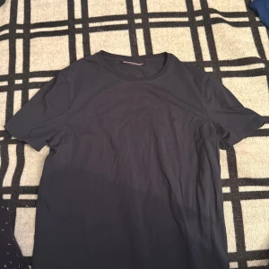 Svart t-shirt från Morris Stockholm - Snygg svart t-shirt från Morris Stockholm i storlek L. Klassisk rund hals och diskret logga på bröstet. T-shirten har korta ärmar och är gjord i mjuk bomull som känns skön mot huden. Perfekt för dig som gillar stilrena och enkla plagg.