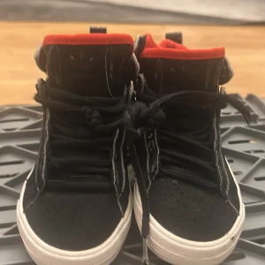 Svarta Adidas sneakers med röd insida - Säljer ett par svarta Adidas sneakers med högt skaft och vit sula. Skorna har röd meshfoder på insidan och klassisk snörning framtill. Adidas-logga syns på plösen och sidan av sulan. Perfekta för dig som gillar streetstyle och vill sticka ut med färgdetaljer.