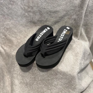 Svarta platåsandaler från ZMISTUO - Säljer ett par svarta sandaler med platåsula från ZMISTUO. De har breda, mjuka tygremmar och en rund tå. Sulan är tjock och har mönstrad undersida för extra grepp. Perfekta för dig som gillar enkel och stilren design med lite höjd.