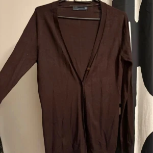 Brun kofta från Zara med knappar - Mörkbrun, tunn kofta från Zara med långa ärmar och flera knappar framtill. Enkel och stilren design, perfekt att slänga över en t-shirt. Materialet är en mix av viskos och polyamid som känns mjuk mot huden. Använd 3 gånger bara 