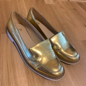 Guldiga metallic loafers från NLY - Säljer ett par riktigt snygga loafers i metallic guld från NLY. Knappt använda!