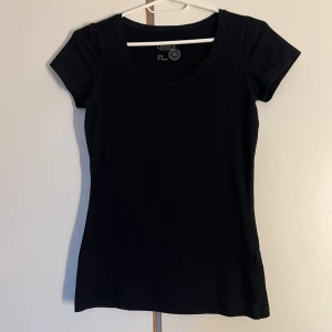 Svart kortärmad topp från Lindex XS - En svart, enkel och stilren kortärmad topp från Lindex i ekologisk bomull. Modellen har rund halsringning och en figurnära passform som funkar till allt. Perfekt basplagg i garderoben för dig som gillar minimalistisk stil.