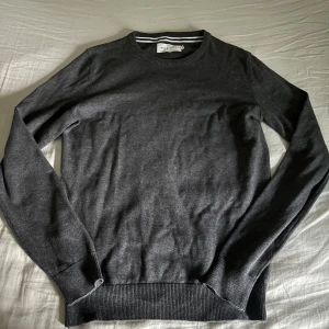 Mörkgrå tröja från Pier One - En stilren mörkgrå tröja från Pier One med rund halsringning och ribbade muddar vid ärmslut och nederkant. Perfekt för lager-på-lager och funkar året runt. Enkel design som är lätt att matcha med olika outfits.