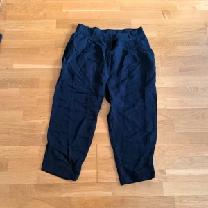 Svarta linnebyxor från H&M - Snygga svarta linnebyxor från H&M i avslappnad modell med croppad längd. Byxorna har dragkedja, knapp och hyskknäppning i midjan samt fickor fram och bak. Perfekta för en chill och stilren look under varmare dagar.