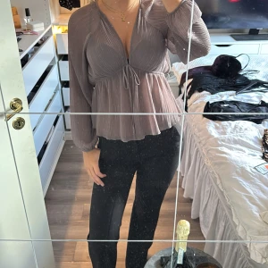 Plisserad lila blus med knyt - Säljer en snygg lila plisserad blus med v-ringning och knyt under bysten. Blusen har långa, luftiga ärmar och ett flowy fall nedtill. Perfekt för dig som gillar en feminin och trendig look.