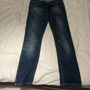  Nudie Jeans  - Säljer ett par klassiska blå jeans från Nudie jeans co Jeansen har raka ben och normal passform, med ikoniska bakfickor med vågig söm och läderpatch med logga. Perfekta för dig som gillar stilrena och tidlösa jeans. Kan gå ner i pris. Stl M 30/32
