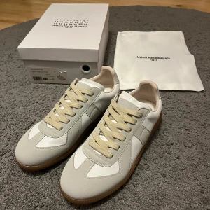 Maison Margiela Gats - Maison Margiela gats i vitt och beige med klassisk gummisula. Skorna har en stilren design med snörning. Perfekta för dig som gillar minimalistisk och lyxig streetstyle.
