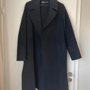 Svart kappa från Zara med klassisk krage - Stilren svart kappa från Zara med klassisk krage och raka linjer. Lång modell med diskreta fickor på sidorna och snyggt fall. Perfekt för dig som gillar minimalistisk och tidlös stil.