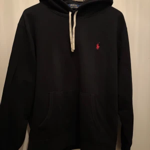 Polo ralph lauren hoodie  - Svart hoodie från Polo Ralph Lauren med klassisk röd logobrodyr på bröstet. Tröjan har huva med vit snörning och en stor magficka framtill. Mjuk bomullskvalitet och långärmad modell, perfekt för kallare dagar. Nypris ligger på 1800, den är sparsamt andvänd och visar inga tecken på andvädning . Tveka inte att höra dig vid frågor 🤩