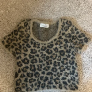 Leopardmönstrad fluffig tröja H&M - Supermjuk och fluffig kortärmad tröja från H&M med leopardmönster i beige och svart. Tröjan har rund halsringning och är perfekt för dig som vill sticka ut med en cool och trendig look. Materialet är lurvigt och känns riktigt mysigt mot huden.
