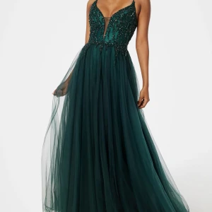 Mörkgrön balklänning med pärlor - Magisk mörkgrön långklänning med djup v-ringning, tunna axelband och snörning i ryggen. Klänningen är dekorerad med glittrande pärlor och kjolen är i flera lager tyll för en riktigt drömmig look. Perfekt för bal eller student! Materialet är troligtvis polyester/tyll, varan har används endast en gång och nypris är  4 699kr, det medföljer också en grön sjal till klänningen!❤️ skriv om ni vill ha mer bilder!