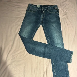 Replay Luz jeans blå, storlek 27/32 - Snygga Replay Luz jeans i klassisk blå tvätt med raka ben och fem fickor. Modellen har normal passform och subtila slitningar för en cool look. Midjan är midwaist och materialet är mjukt jeans. Perfekta för dig som gillar stilrena och tidlösa jeans.