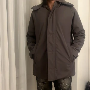 Olivgrön quiltad parkajacka Henry Lloyd  - Snygg grön parkajacka från Henry Lloyd Consort med quiltat foder och huva. Jackan har en stilren design med dold dragkedja.