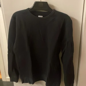 Svart sweatshirt från C.P. Company - Svart sweatshirt från C.P. Company med klassisk rund hals och lång ärm. Tröjan har den ikoniska linsen på ena ärmen och är tillverkad i mjuk bomull. Perfekt för dig som gillar stilrena och snygga streetwear-plagg.