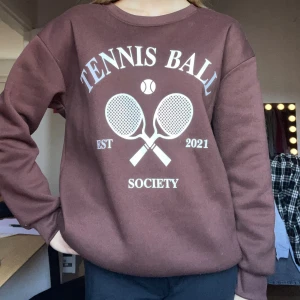 Brun sweatshirt🤎 - Brun sweatshirt med vit tryck framtill, där det står 'Tennis Ball Society' och har två korsade tennisrack och en boll. Rund halsringning och långa ärmar med ribbade muddar. Mjuk och skön, använd fåtal gånger.