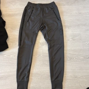 Nike Air Max grå mjukisbyxor S - Snygga grå mjukisbyxor från Nike Air Max med svarta detaljer och dragkedjor på fickorna. Byxorna har elastisk midja, smal passform och Air Max-logga längs benen. Perfekta för chill eller träning.