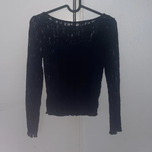 Svart spetsblus från Kappahl - Svart långärmad blus från Kappahl i transparent spetsmaterial. Toppen har en rund halsringning och smal passform, perfekt för att ge en cool och elegant touch till din outfit.