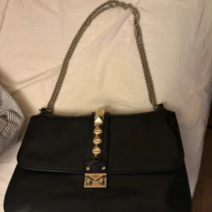 Svart axelväska Valentino med nitar - HAR KVAR BOX!!💓💓💓mötts upp i Stockholm 💓💓💓Snygg svart axelväska från Valentino i skinn med kedjerem i guldfärg. 💓Väskan är modellen glam lock. Den har guldiga pyramidnitar på locket och ett väsk lås framtill. Perfekt väska till skolan då det är den större modellen så får plats med mycket  i den💓💓 kan sänka priset vid snabbt köp 
