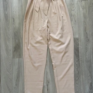 Beige byxor med bälte från NLY Trend - Beige byxa från NLY Trend (Nelly) i storlek 32. Modellen är högmidjad med ett matchande bälte i midjan och har ett mjukt material. Tyvärr för långa för mig💞hör av dig vid frågor!