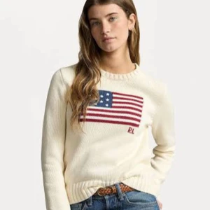 Vit stickad tröja från Ralph Lauren - Säljer en vit stickad tröja från Ralph Lauren med amerikansk flagga och RL-broderi på bröstet. Tröjan har rund halsringning, långa ärmar och ribbade muddar. Perfekt för dig som gillar klassisk och preppy stil.