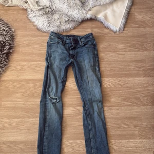 Blå skinny jeans Jack & Jones 28/30 - Säljer ett par blå skinny jeans från Jack & Jones i storlek 28/30. Jeansen har klassisk femficksdesign, slitningar och ett hål på ena knät för en cool, avslappnad look. Tillverkade i mjukt denimtyg med snygga detaljer och normal passform i midjan.