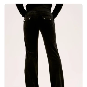 Svarta velourbyxor Juicy Couture - Svarta mjukisbyxor från Juicy Couture i mjuk velour med snörning i midjan och fickor både fram och bak. Byxorna har en relaxed passform och raka ben, perfekta för en chill och trendig look.