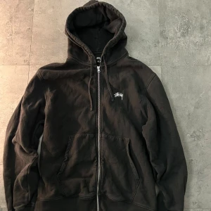 Svart Stüssy hoodie med dragkedja, storlek  XL - Svart hoodie från Stüssy i storlek XL, tillverkad i 100% bomull. Tröjan har huva med snörning, två stora fickor fram och en grov dragkedja. Stüssy-logga broderad på bröstet. Perfekt för dem som gillar streetwear och lite casual stil. Pris kan diskuteras:)