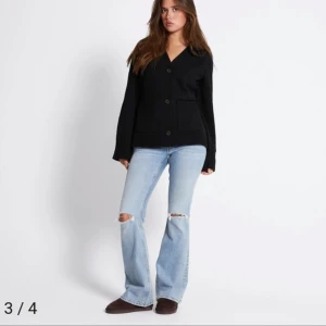 Svart kofta från 157 med knappar - Svart stickad kofta från 157 med v-ringning, stora knappar framtill och två rejäla fickor. Koftan har långärmad passform och ribbade muddar vid ärmslut och fickor. Perfekt för lager-på-lager och chill vibes.